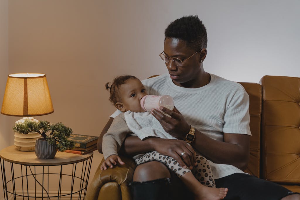 A Man Sitting on Sofa While Feeding a Toddler