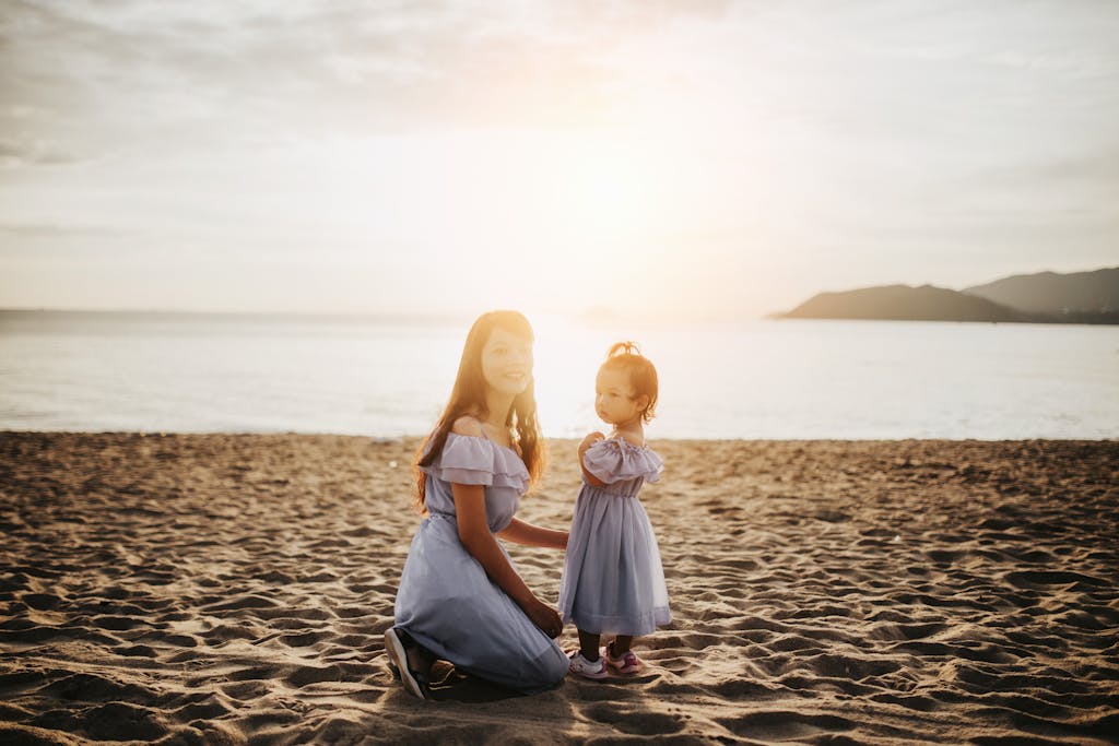 A mother and daughter share a tender moment on the beach at sunset, capturing the essence of love and nature.